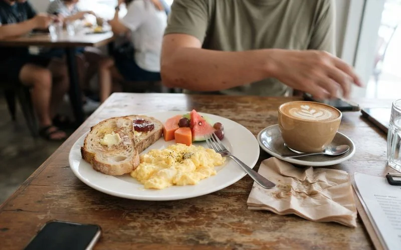 A brunch plate with eggs, toast, and greens on a wooden table at a western-style cafe in Ipoh, morning light through a window